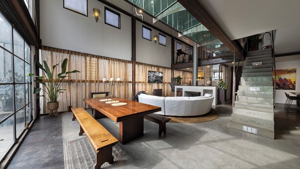 A spacious interior with a high ceiling, a wooden dining table, a white sofa, and a staircase leading to an upper level. - Melbourne City Apartments Luxury Loft House with rooftop (Southbank)