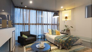 A modern bedroom with a sofa, a bed with a colorful blanket, a coffee table with a tray, and a large window with curtains. - Melbourne City Apartments Luxury Loft House with rooftop (Southbank)