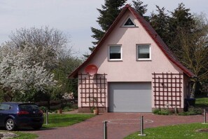 A single-story building with a garage door, a satellite dish, and a small garden area with a car parked in front. - Holiday apartment with 1 bedroom (Vielist)