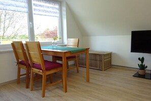 A room with a dining table, chairs, a television, a window, and a plant. - Holiday apartment with 1 bedroom (Vielist)