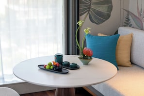 Ein runder Tisch mit weißer Oberfläche, eine grüne Vase mit einer roten Blume sowie ein Teller mit Trauben und Tomaten.