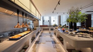 Un espace de restauration moderne dans un hôtel, doté de plusieurs buffets, d’un comptoir central de service et d’une grande fenêtre laissant entrer la lumière naturelle.