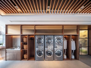 A modern laundry room with four stacked front-loading washing machines, wooden shelving, and a built-in sink. - SSAW Hotel Hefei Feixi University Town (Hefei)
