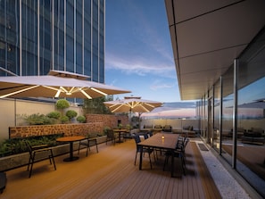 An outdoor patio area with tables and chairs, umbrellas, and a view of the city skyline.