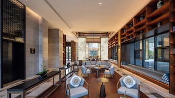 Un interior moderno con una zona de estar, estanterías de madera y grandes ventanales.
