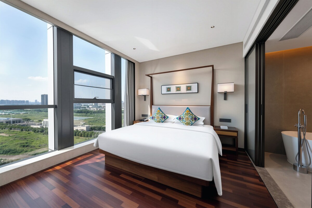 A modern hotel room with a large bed, a view of the city, and a separate bathroom area.