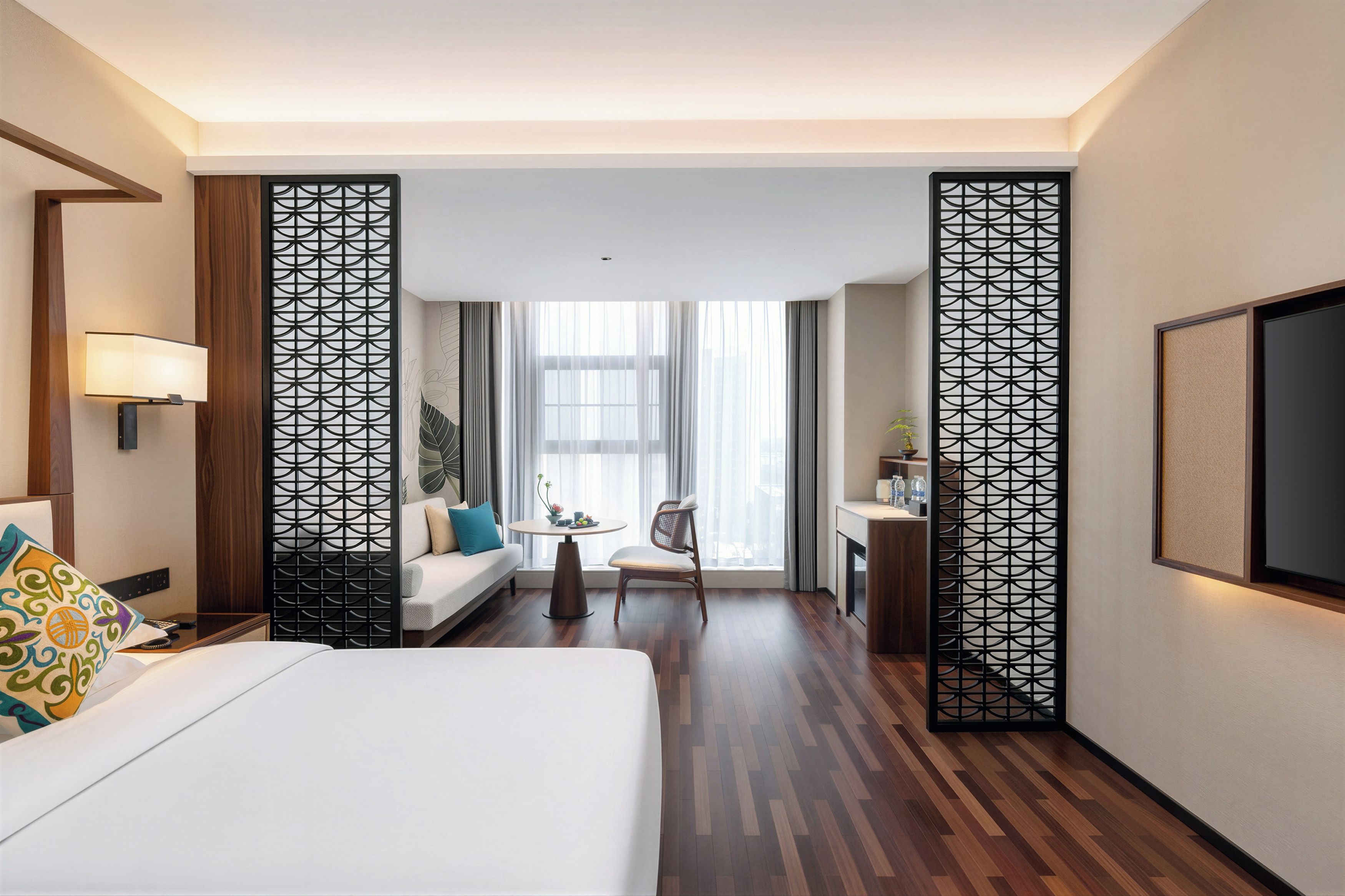 A hotel room with a bed, a desk, a chair, a TV, and a large window with curtains.