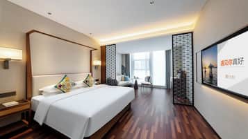 Habitación de hotel con una cama grande, mesitas de noche, zona de estar con sofá y sillones, y un ventanal amplio.