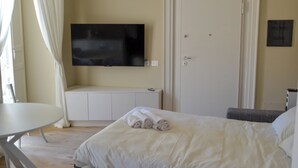 Ett hotellrum med en säng, en tv som är monterad på väggen, en dörr och ett litet bord.