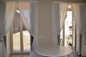 A room with a round table and two chairs, large windows with white curtains, and a view of a tiled patio outside. - Catania historic center, 3bedrooms + 2 bathrooms noble 200sq. meters apartment (Catania)