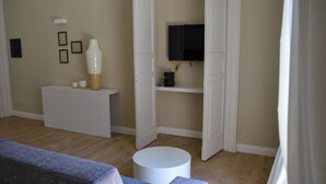 Ett vardagsrum med en soffa, ett vitt soffbord, en tv som är monterad på väggen och en dörr som leder till ett annat rum.