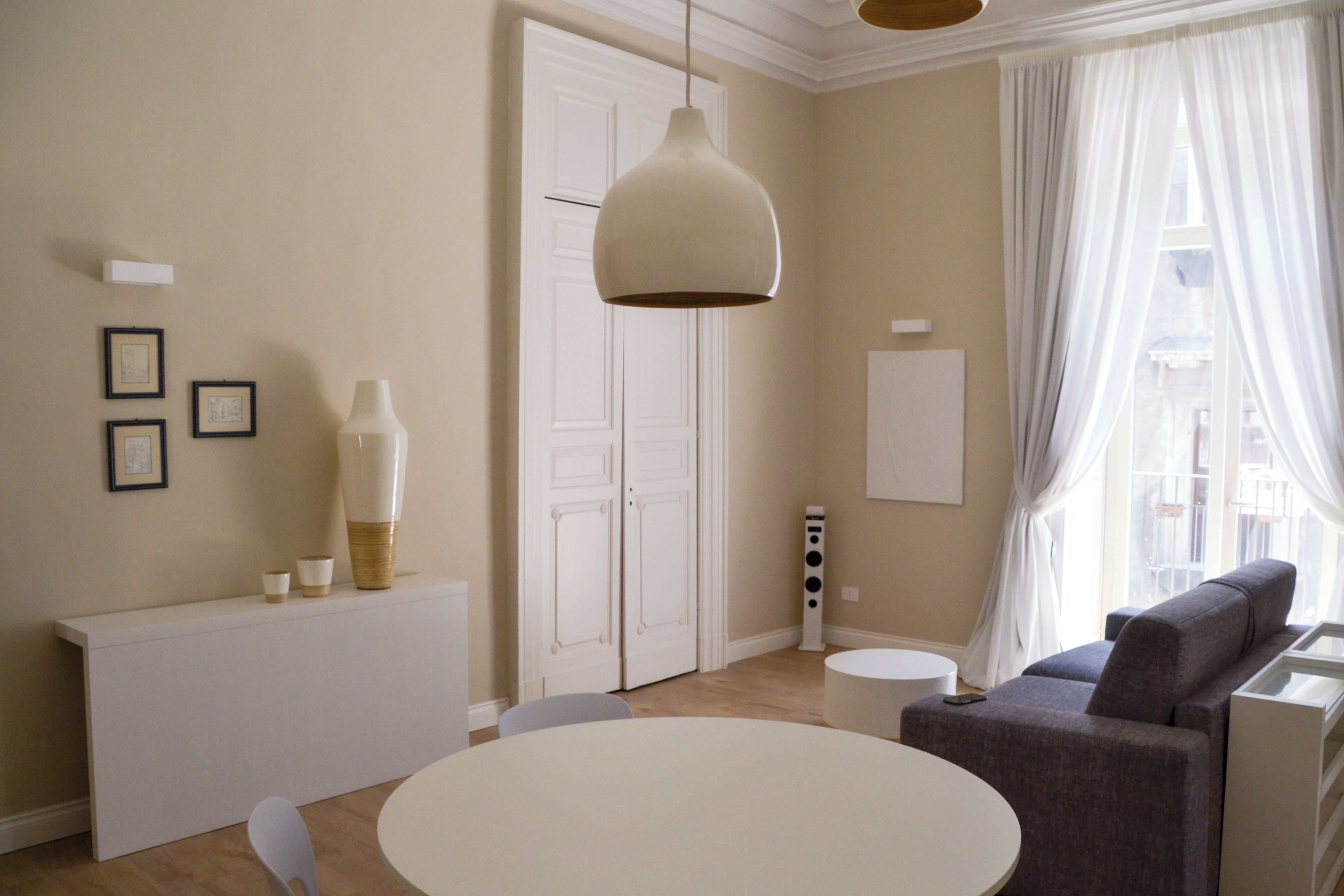 A modern living room with a round white table, a grey sofa, and a pendant light.
