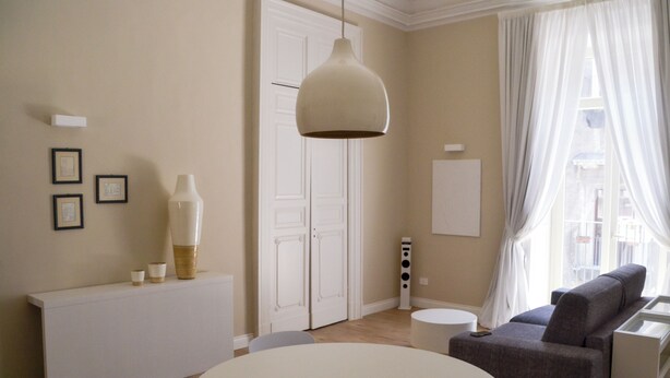 Ett modernt vardagsrum med ett runt, vitt bord, en grå soffa och en hängande lampa.