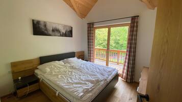 A bedroom with a wooden ceiling, a bed, a nightstand, a painting, and a balcony with curtains.