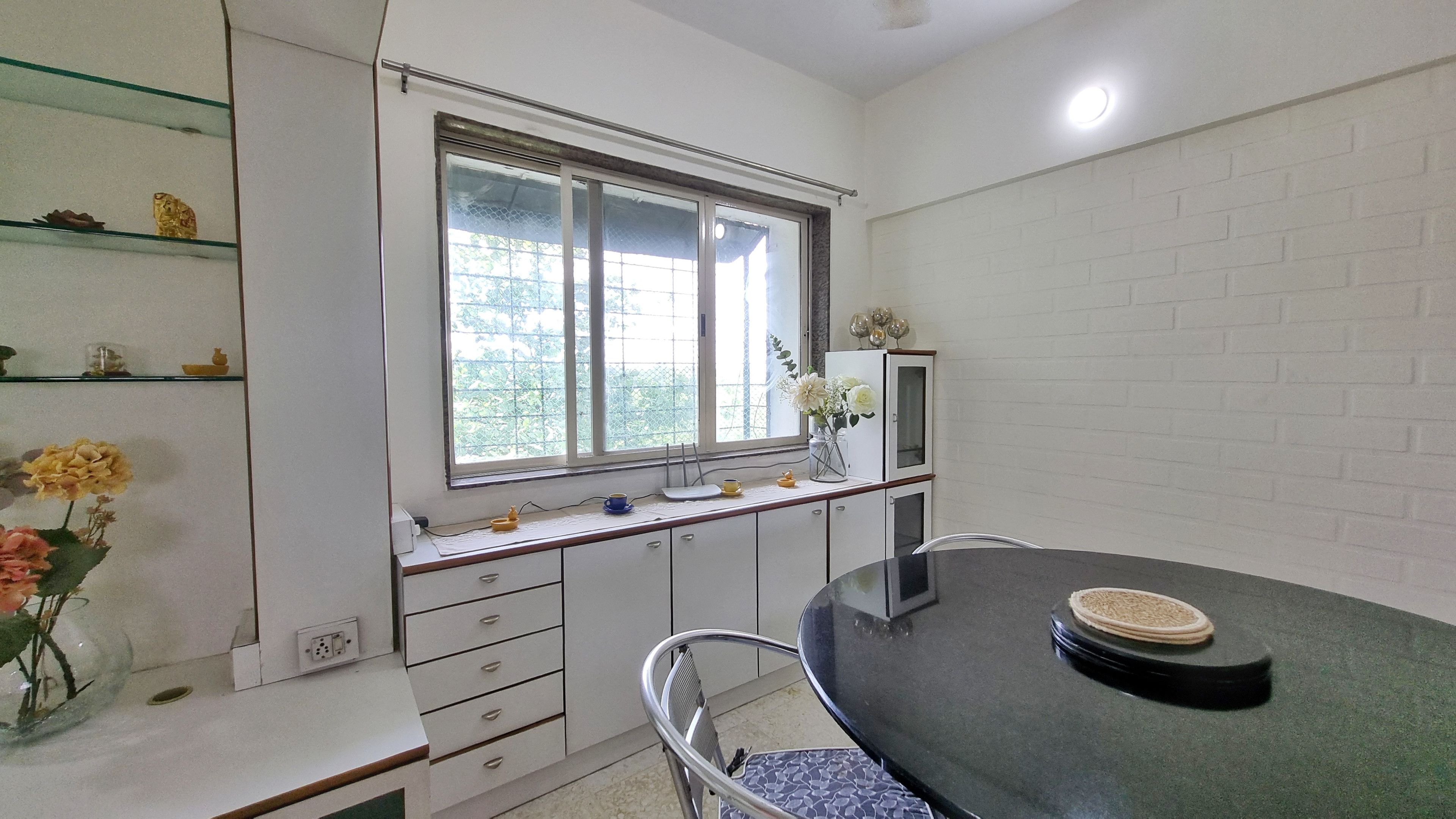 Una habitación con una mesa de comedor, sillas, una ventana con persianas, un estante con adornos y un mueble con televisor.