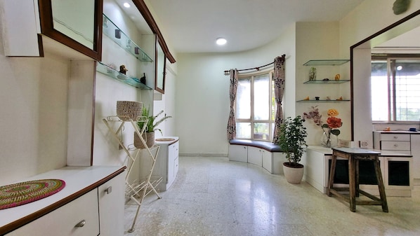 Una habitación con distribución curva, una ventana con cortinas, una estantería con objetos decorativos y una planta en maceta.