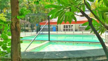 Una piscina con borde de piedra, rodeada de árboles y un edificio con techo rojo.