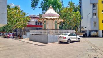 A white car parked in front of a small, white building with a dome roof, surrounded by palm trees and a fence.