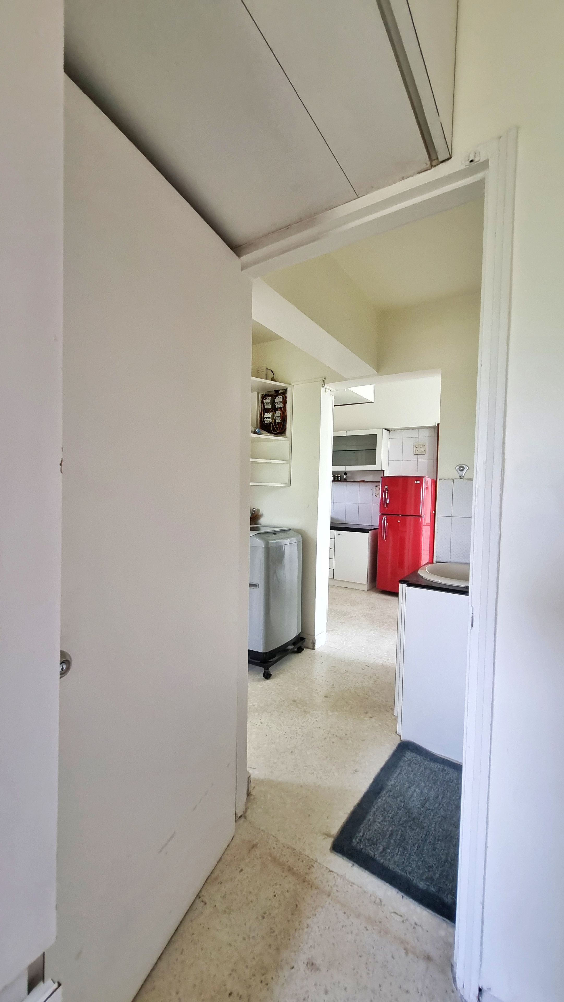 Un estrecho pasillo que da a una zona de cocina con armarios blancos y un refrigerador rojo.