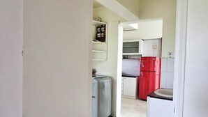 Un estrecho pasillo que da a una zona de cocina con armarios blancos y un refrigerador rojo.