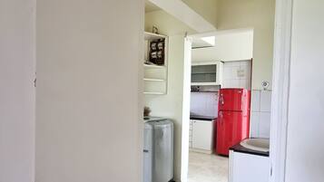 Un estrecho pasillo que da a una zona de cocina con armarios blancos y un refrigerador rojo.