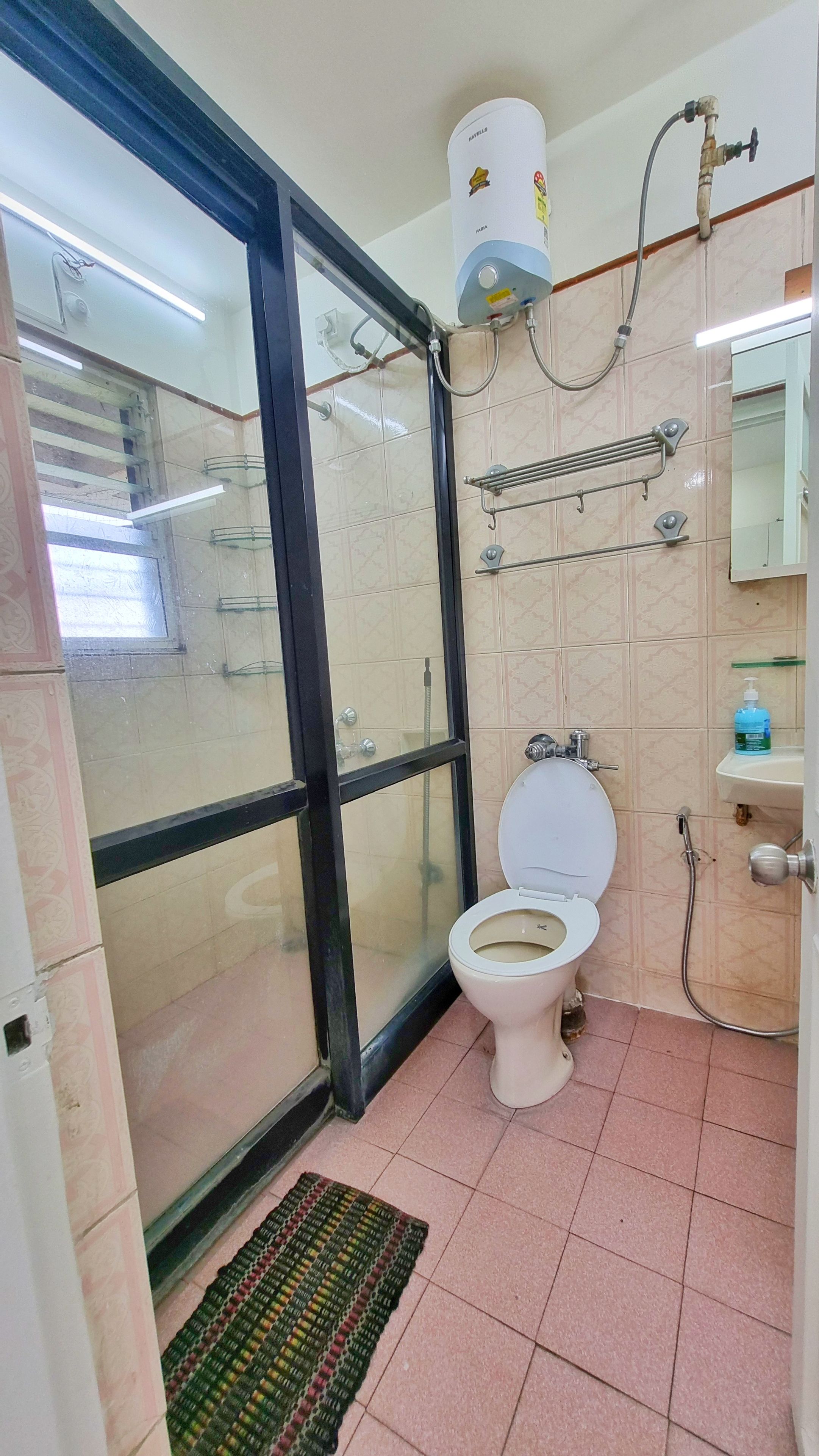 Et badeværelse med toilet, bruser, glasdør, bøjlestang til håndklæder og vask med sæbedispenser.