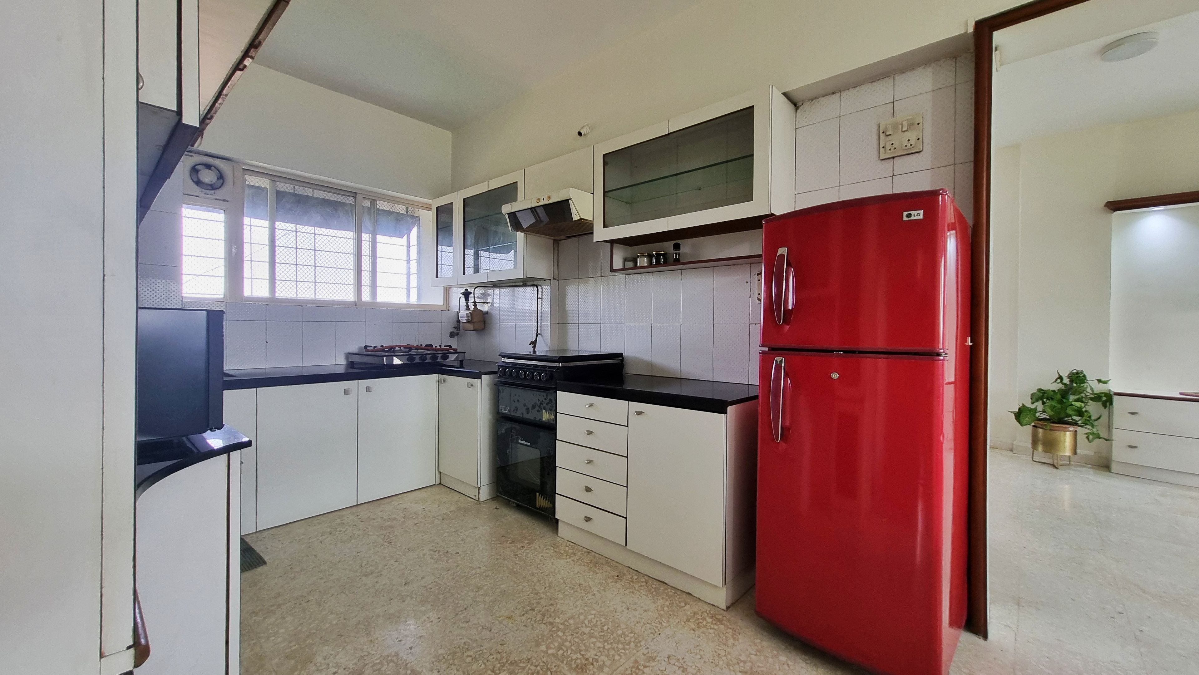 Una cocina con armarios blancos, un refrigerador rojo, una estufa y una ventana con persianas.