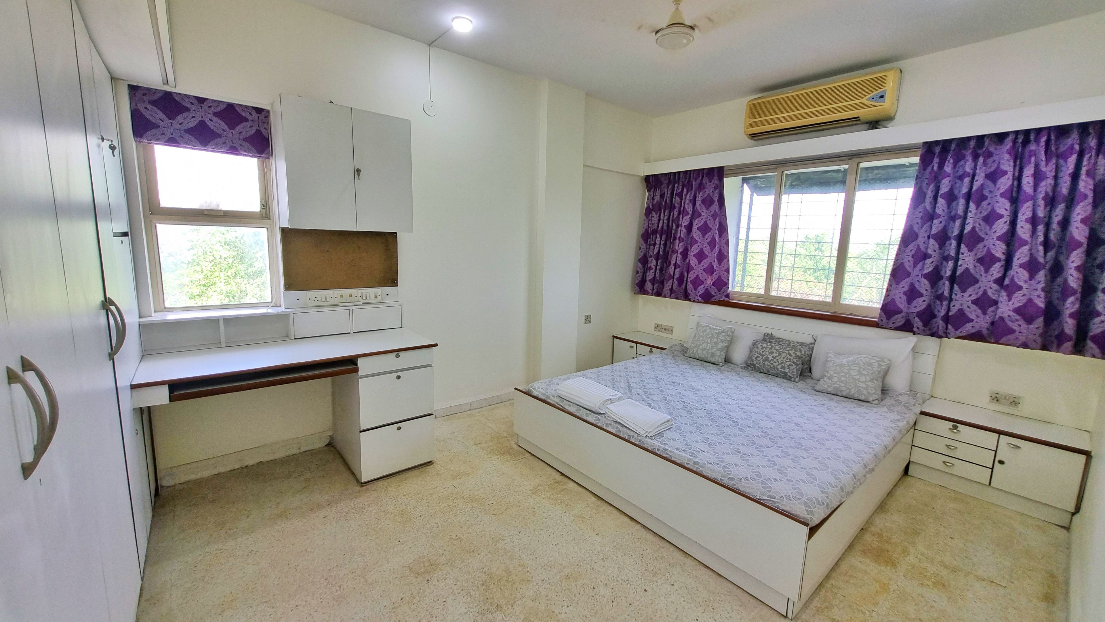 A bedroom with a bed, a desk, a wardrobe, and a window with curtains.