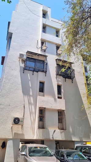 Un edificio de varios pisos con balcones, unidades de aire acondicionado y un estacionamiento con coches.