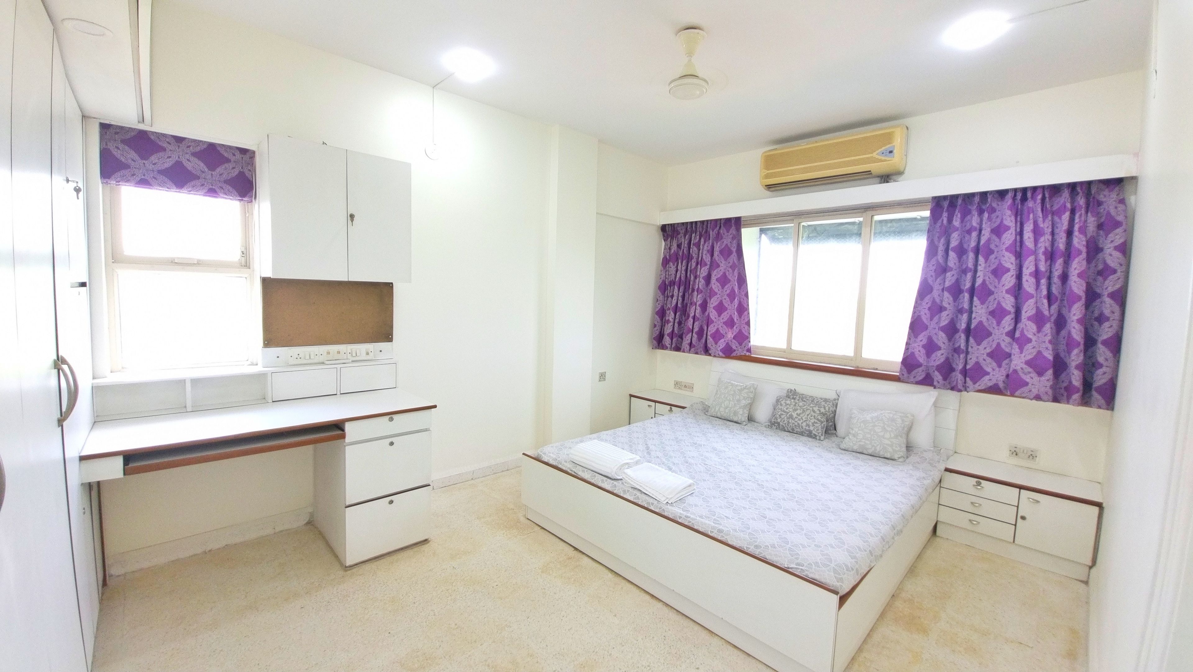 Quarto com cama, escrivaninha, guarda-roupa e janela com cortinas.