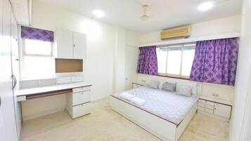 Quarto com cama, escrivaninha, guarda-roupa e janela com cortinas.