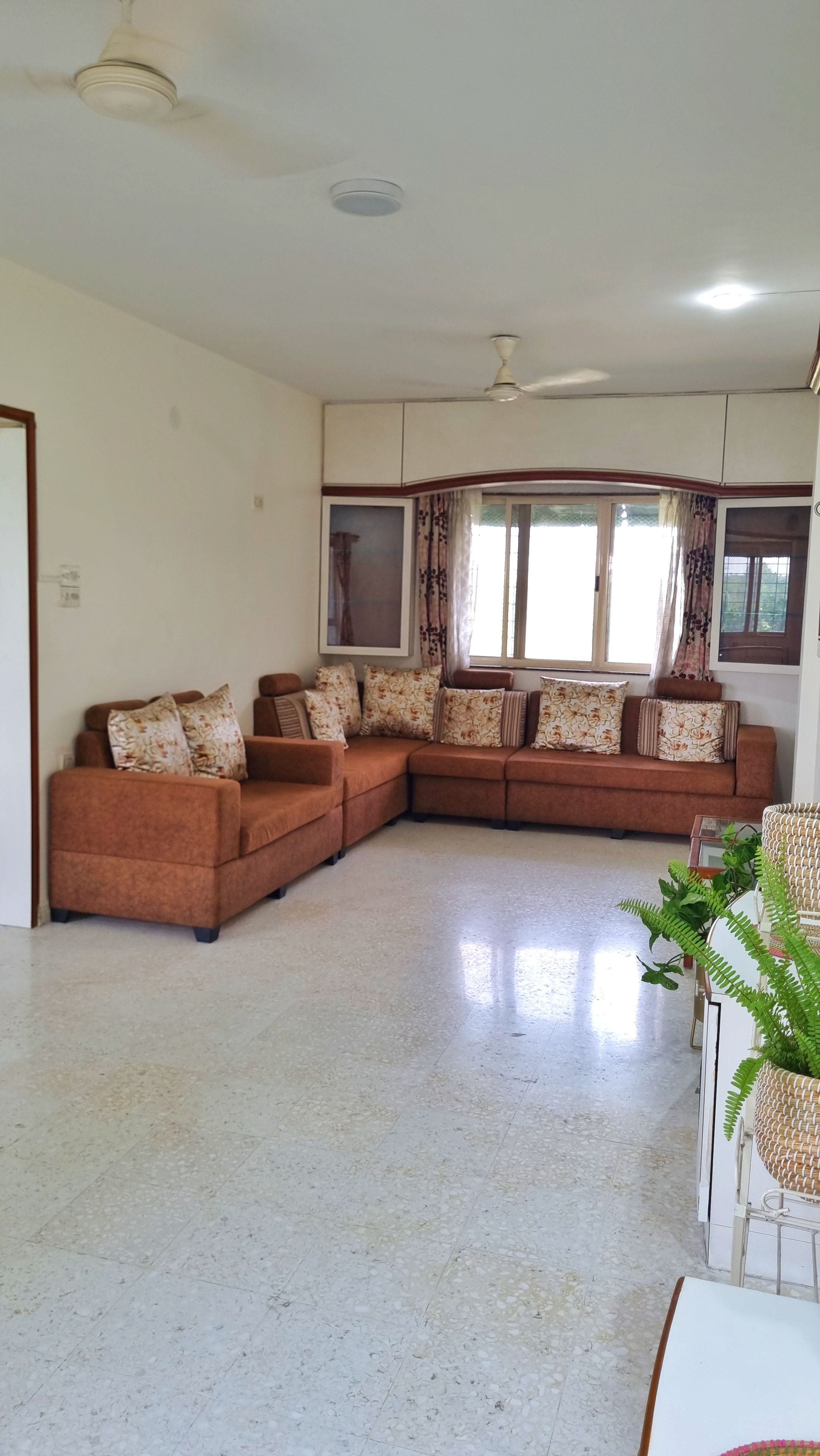 Una sala de estar con un sofá modular, un ventilador de techo y un ventanal con cortinas.