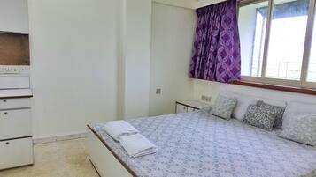A bedroom with a bed, a dresser, a window with curtains, and a ceiling fan.