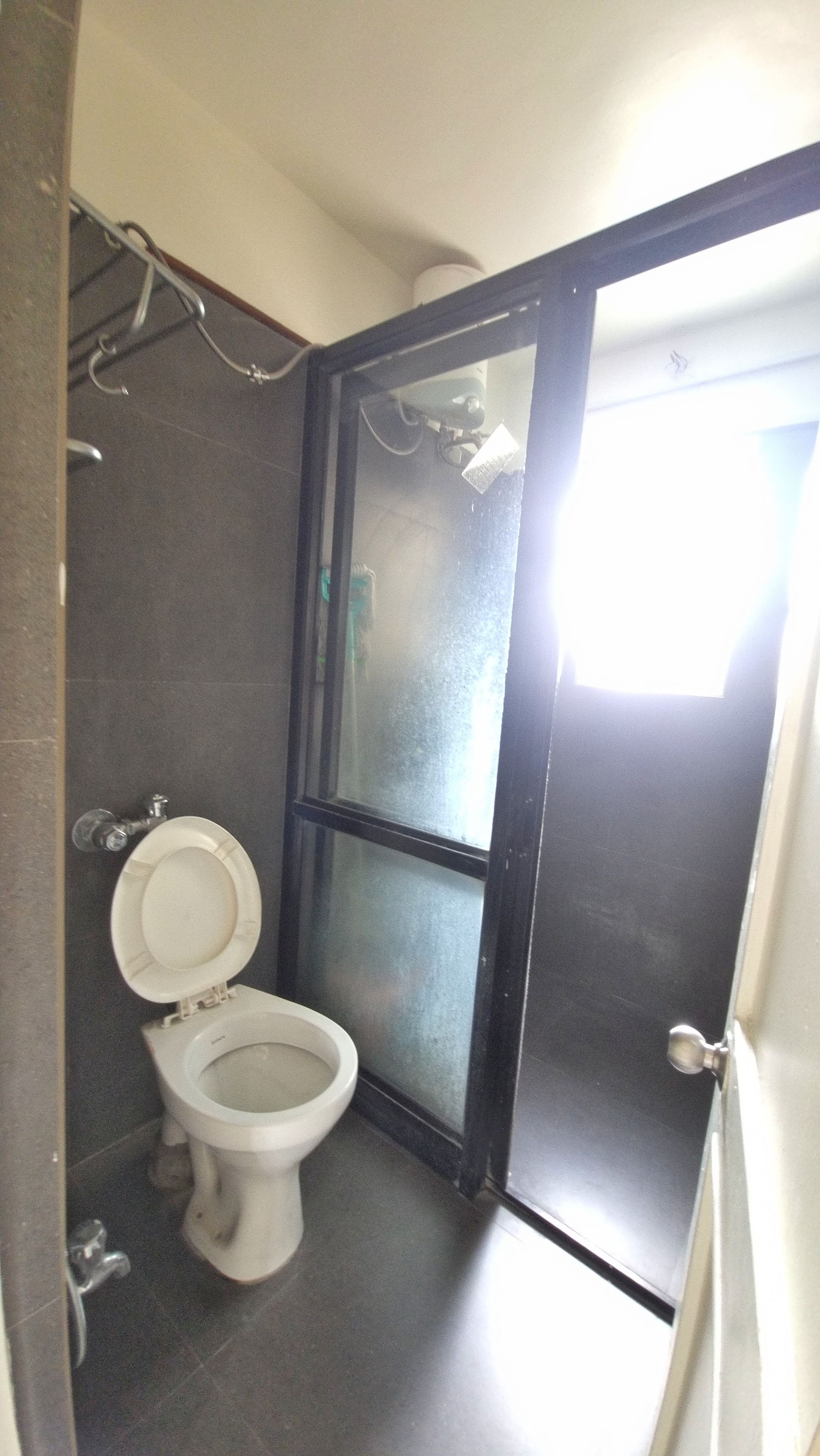 A bathroom with a toilet, a shower area, and a door leading to another room.