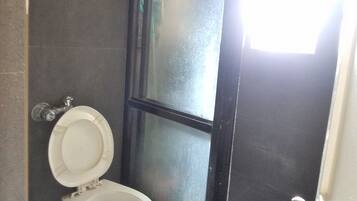 A bathroom with a toilet, a shower area, and a door leading to another room.