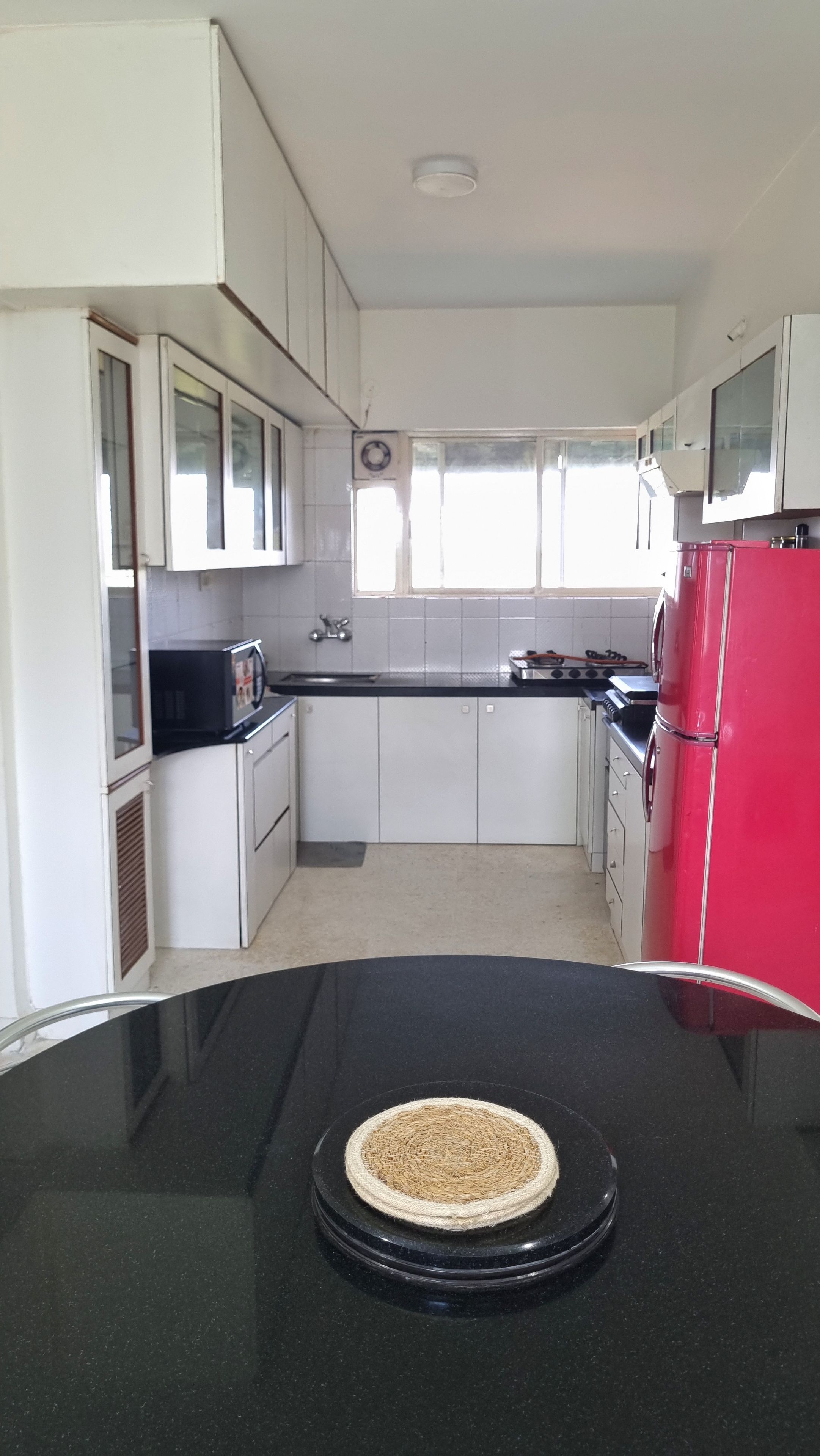 A kitchen with white cabinets, a black countertop, a red refrigerator, and a window with blinds.