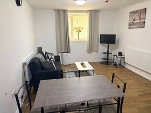 A living room with a sofa, a coffee table, a TV, and a window with curtains. - Beautiful 3-Bedroom Flat in the heart of Swansea (Swansea)