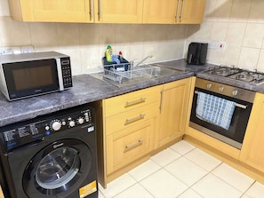 A compact kitchen with a microwave, washing machine, and gas stove. - Beautiful 3-Bedroom Flat in the heart of Swansea (Swansea)