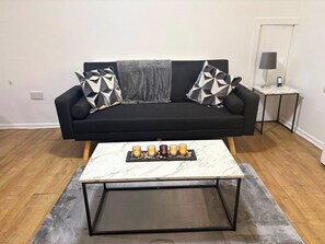 A modern living room with a black sofa, a marble coffee table, and a small side table with a lamp. - Beautiful 3-Bedroom Flat in the heart of Swansea (Swansea)