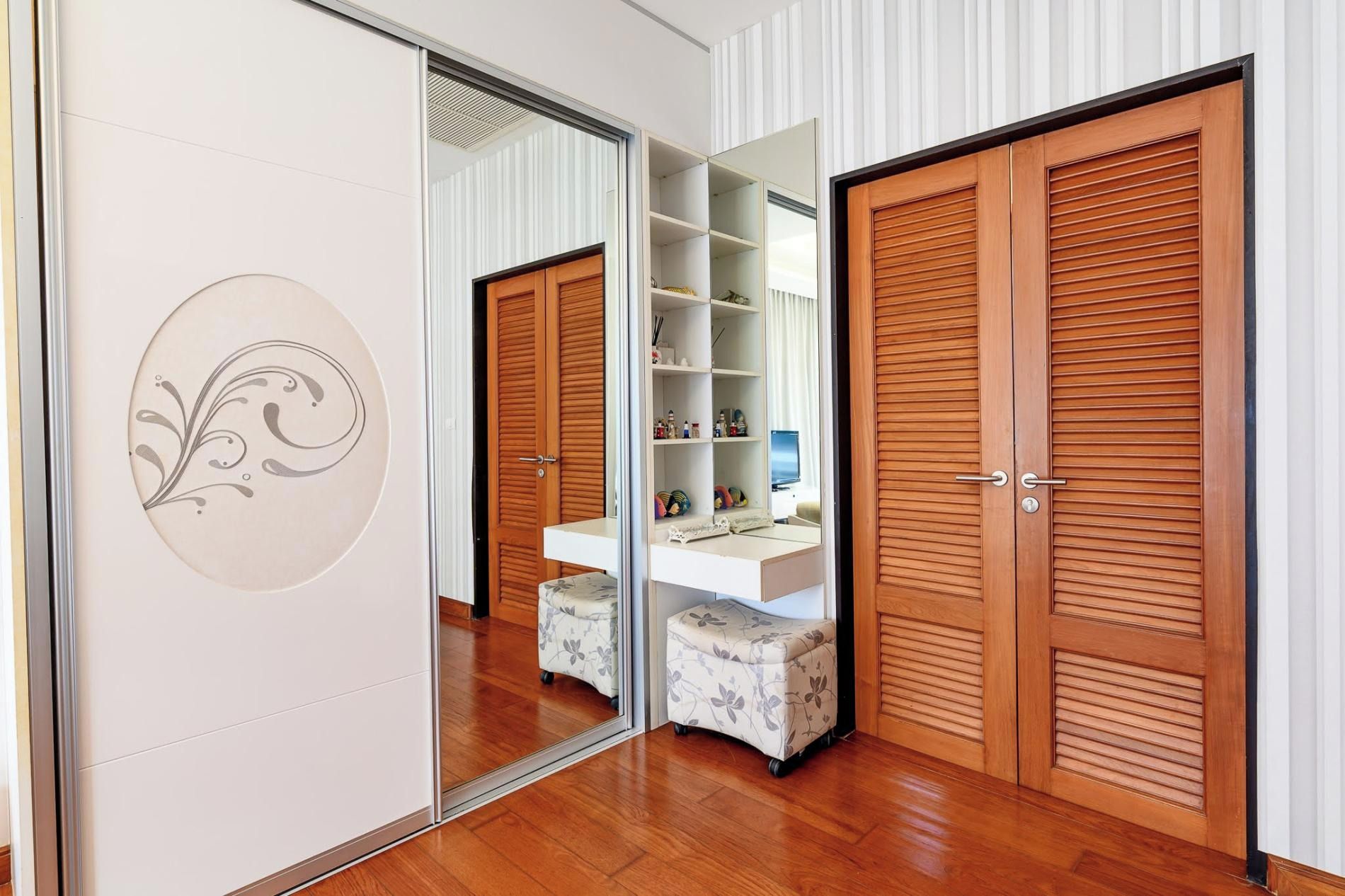 Una habitación con un armario de espejo, una consola blanca y un ropero de madera.