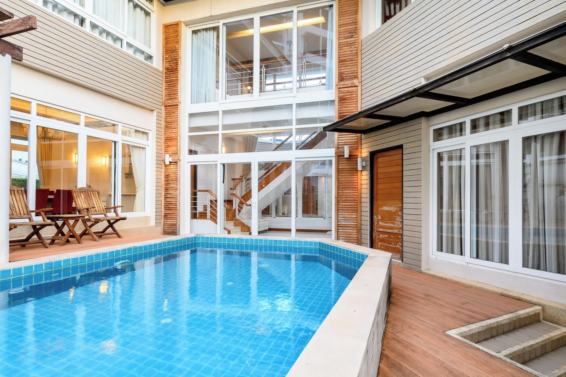 Una piscina interior moderna con cerramiento de vidrio, cubierta de madera y una escalera que conduce a un nivel superior.