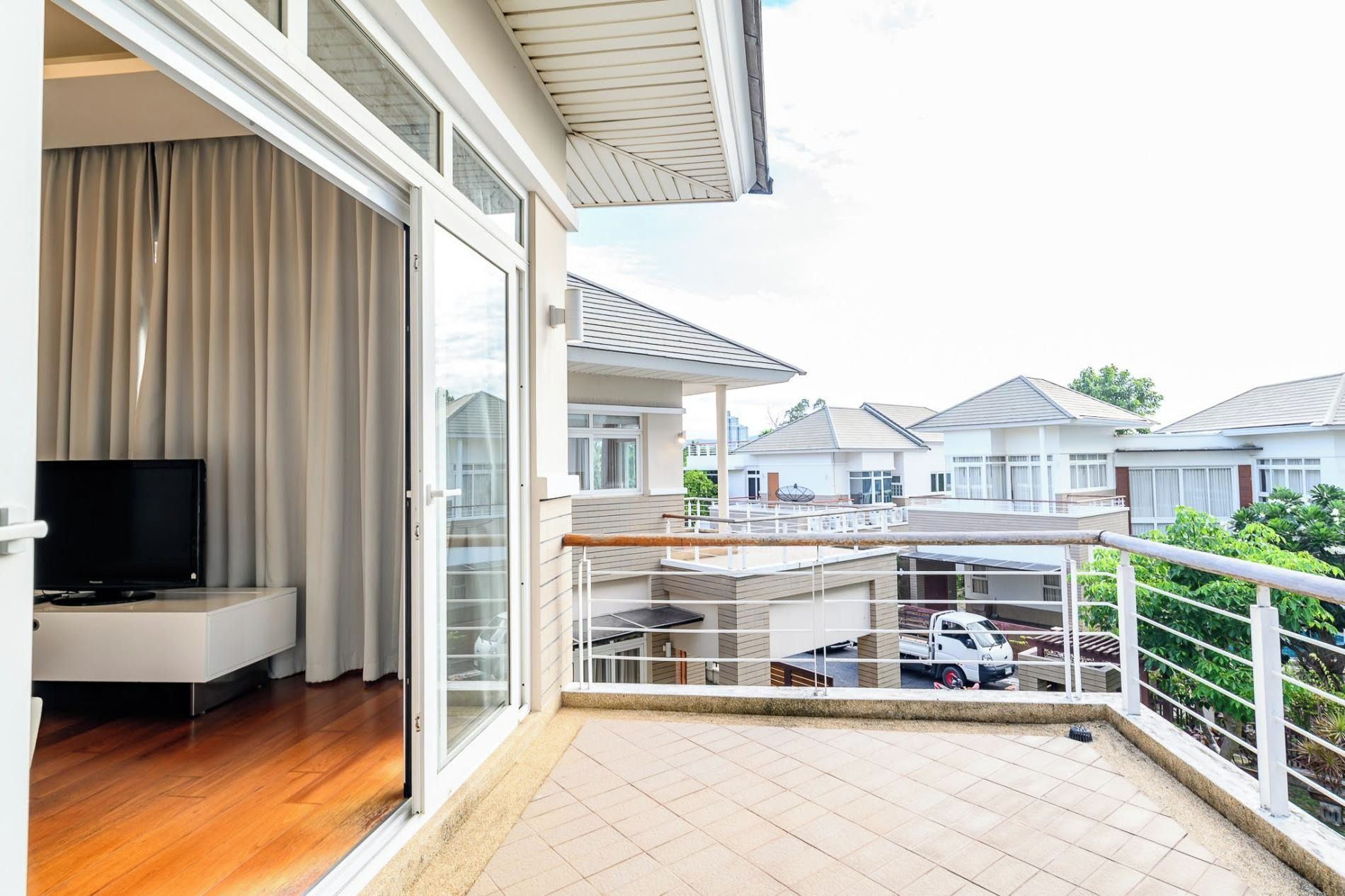 A balcony with a TV, sliding glass doors, and a view of neighboring houses.