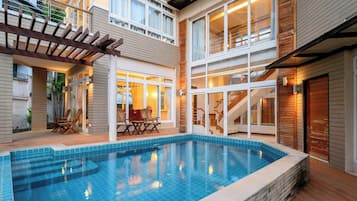 Edifício residencial com piscina, deck de madeira e área de varanda coberta.