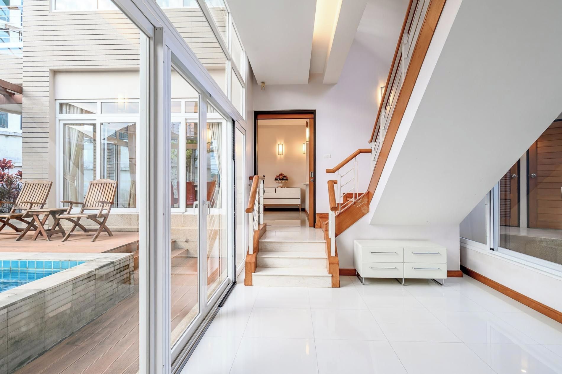 Un interior moderno con un ventanal que da a una zona de piscina, una escalera con barandillas de madera y vistas al exterior.