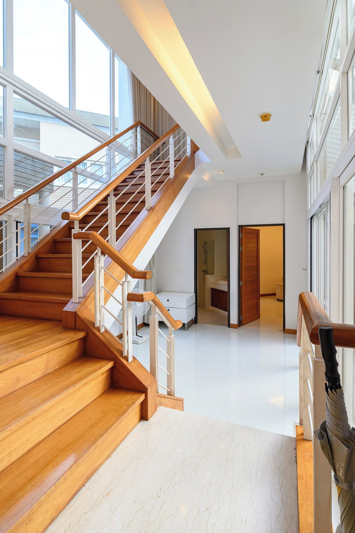 Un interior espacioso con una escalera de madera que conduce a un nivel superior, un gran ventanal y vistas al exterior.