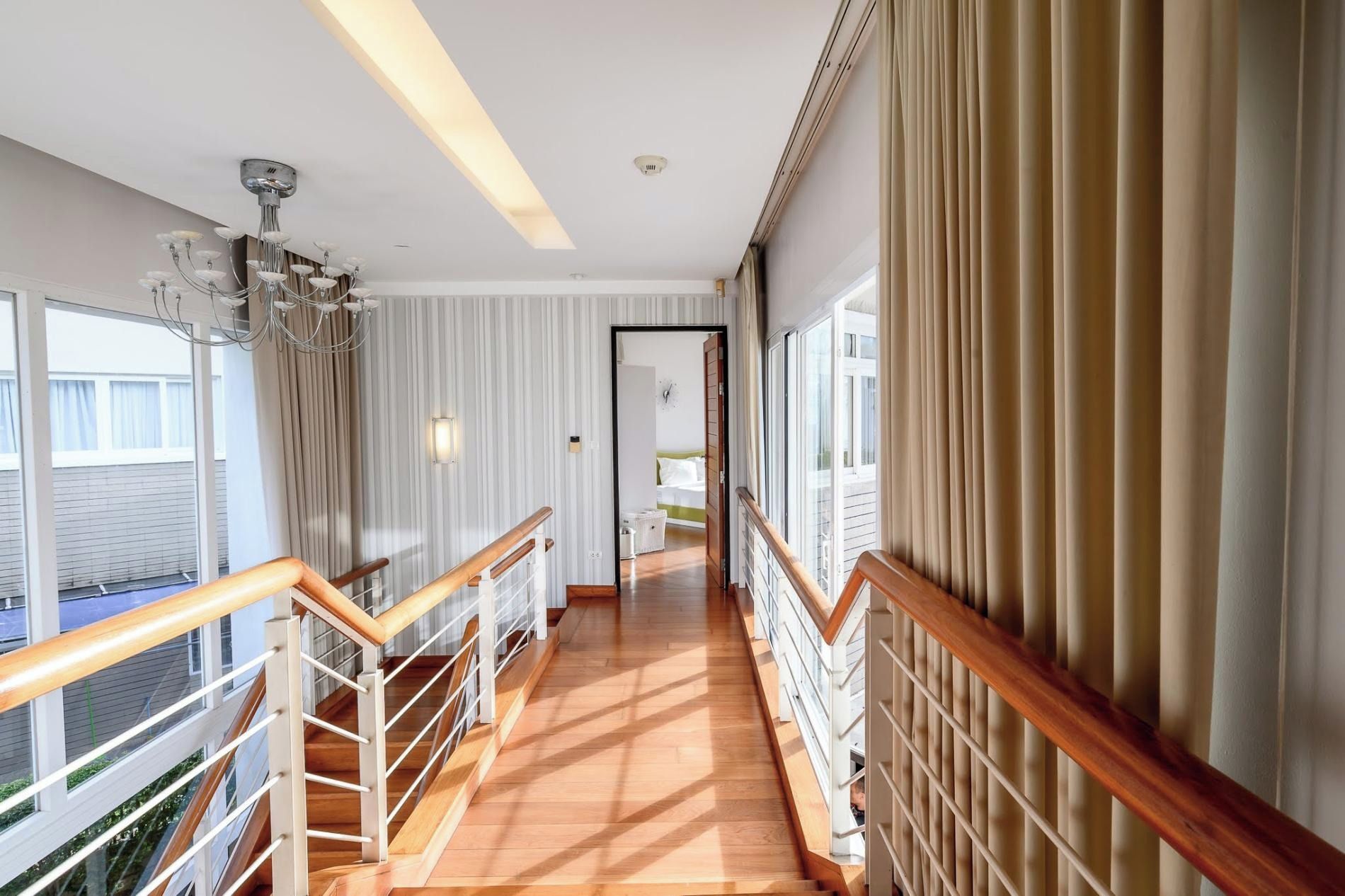 Un pasillo de hotel con una escalera de madera, un candelabro y vistas al exterior.