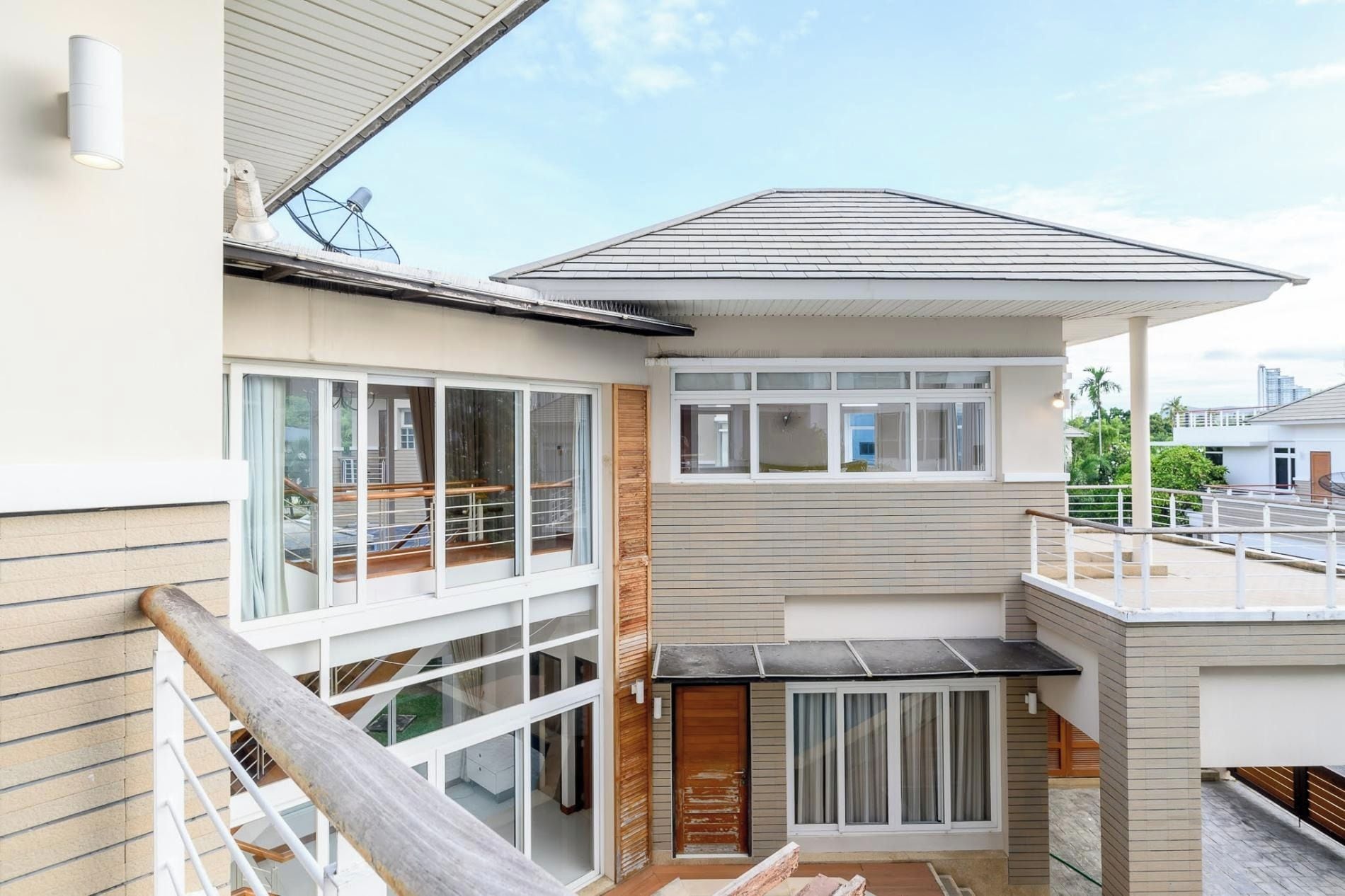 A modern two-story house with a balcony, large windows, and a satellite dish.