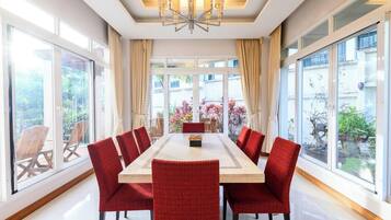 A dining area with a long table and red chairs, large windows, and a chandelier.