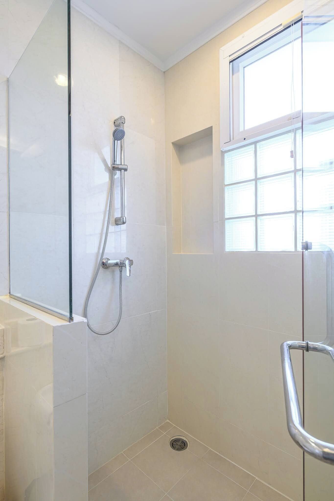 A bathroom with a glass shower enclosure, a window, and a tiled floor.