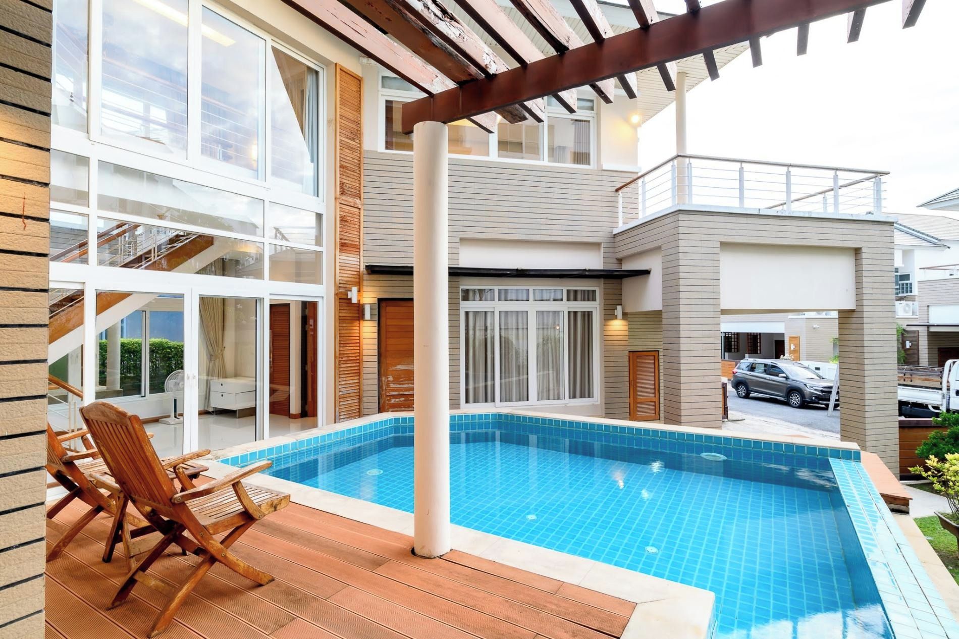 A modern residential building with a swimming pool, wooden deck, and a car parked outside.